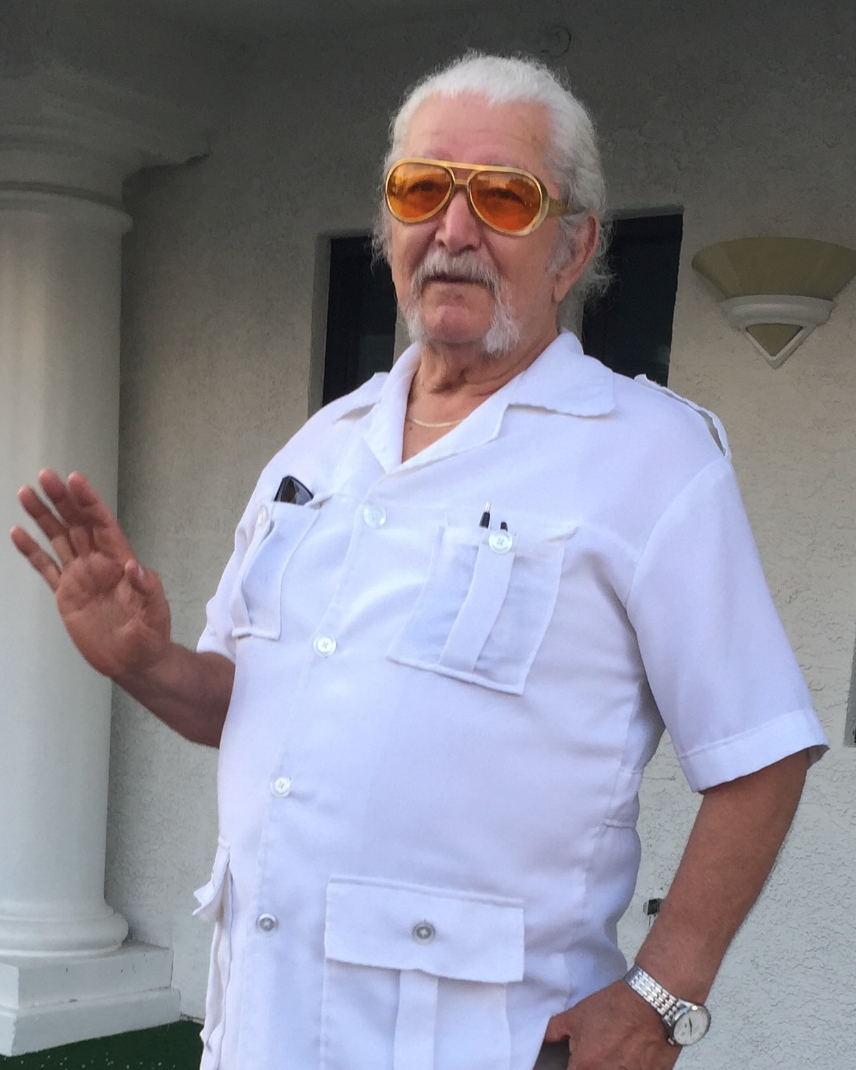 Landon &ldquo;Tata&rdquo; Wellman waving, in a white guayabera and amber aviator sunglasses.